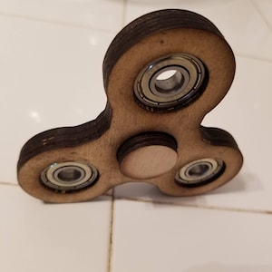 May include: A wooden fidget spinner with three metal bearings. The spinner is brown and has a natural wood finish.