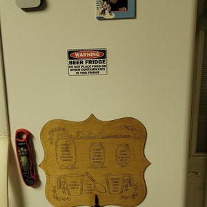May include: A white refrigerator with a wooden sign that says "Kitchen Conversions" with measurements for cups, pints, quarts, and ounces. The sign is attached to the refrigerator with a key ring and keys.