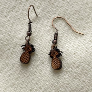 Op de afbeelding: Een paar bruine houten ananas oorbellen met koperkleurige haken.