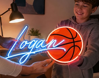 Puede incluir: Un letrero de neón personalizado con el nombre Logan en letras cursivas de color azul brillante, unido a un gráfico circular de baloncesto naranja con líneas negras. El letrero está iluminado y tiene un soporte de acrílico transparente.