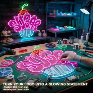 May include: A custom LED neon sign featuring the text THE SUGAR MILL in pink and light blue, shaped like a cupcake with a cherry on top. The sign is displayed on a green work mat alongside tools, wire spools, and a heat gun for assembly.