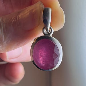 May include: A silver pendant with a large, oval-shaped, faceted, pink gemstone.