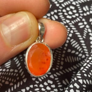 May include: A silver pendant with a bright orange carnelian gemstone. The pendant is oval shaped and has a smooth, polished finish.