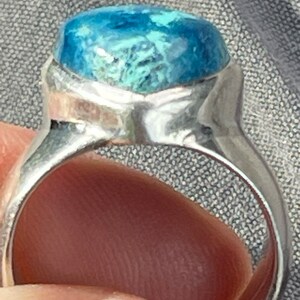 Puede incluir: Un anillo de plata con una piedra preciosa azul y verde engastada en el centro. El anillo est&aacute; hecho de plata de ley y tiene un dise&ntilde;o simple y elegante.