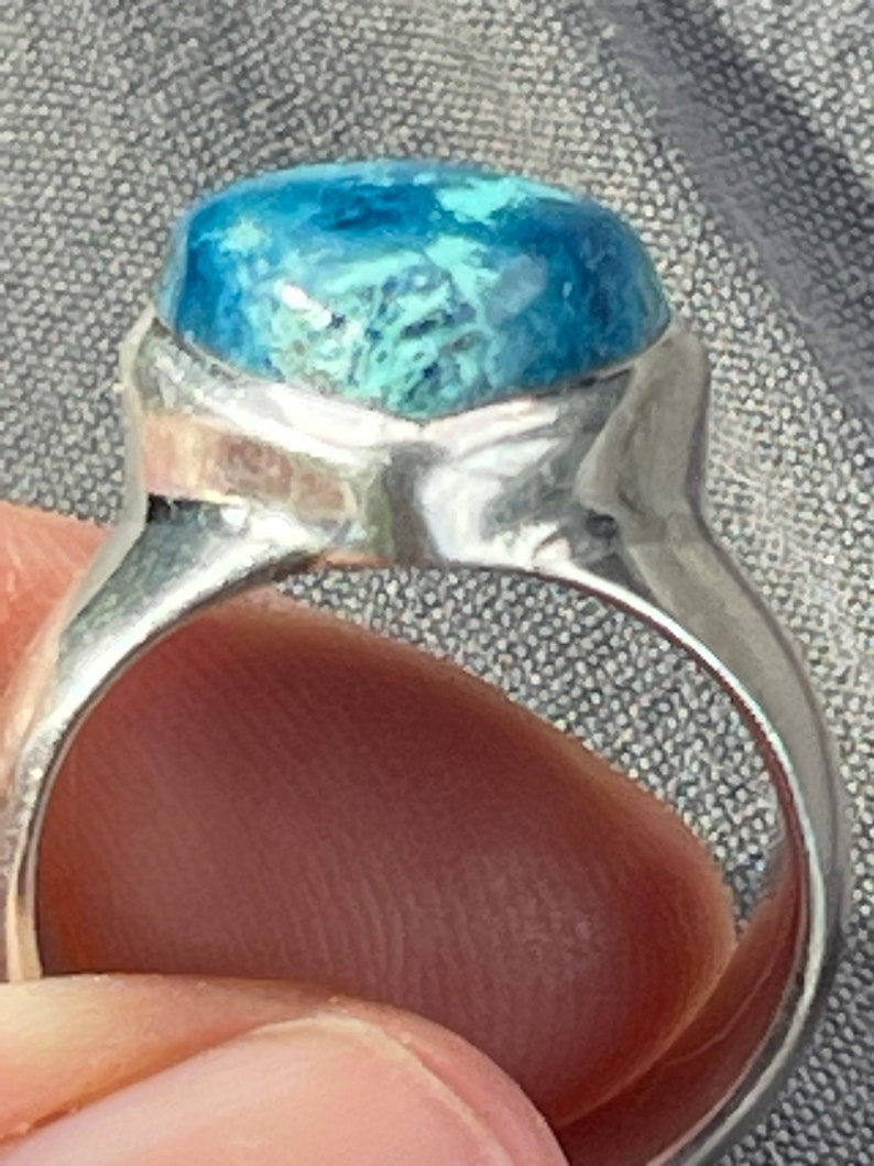 Puede incluir: Un anillo de plata con una piedra preciosa azul y verde engastada en el centro. El anillo est&aacute; hecho de plata de ley y tiene un dise&ntilde;o simple y elegante.