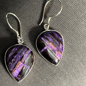 May include: A pair of silver dangle earrings with purple and black teardrop-shaped stones.