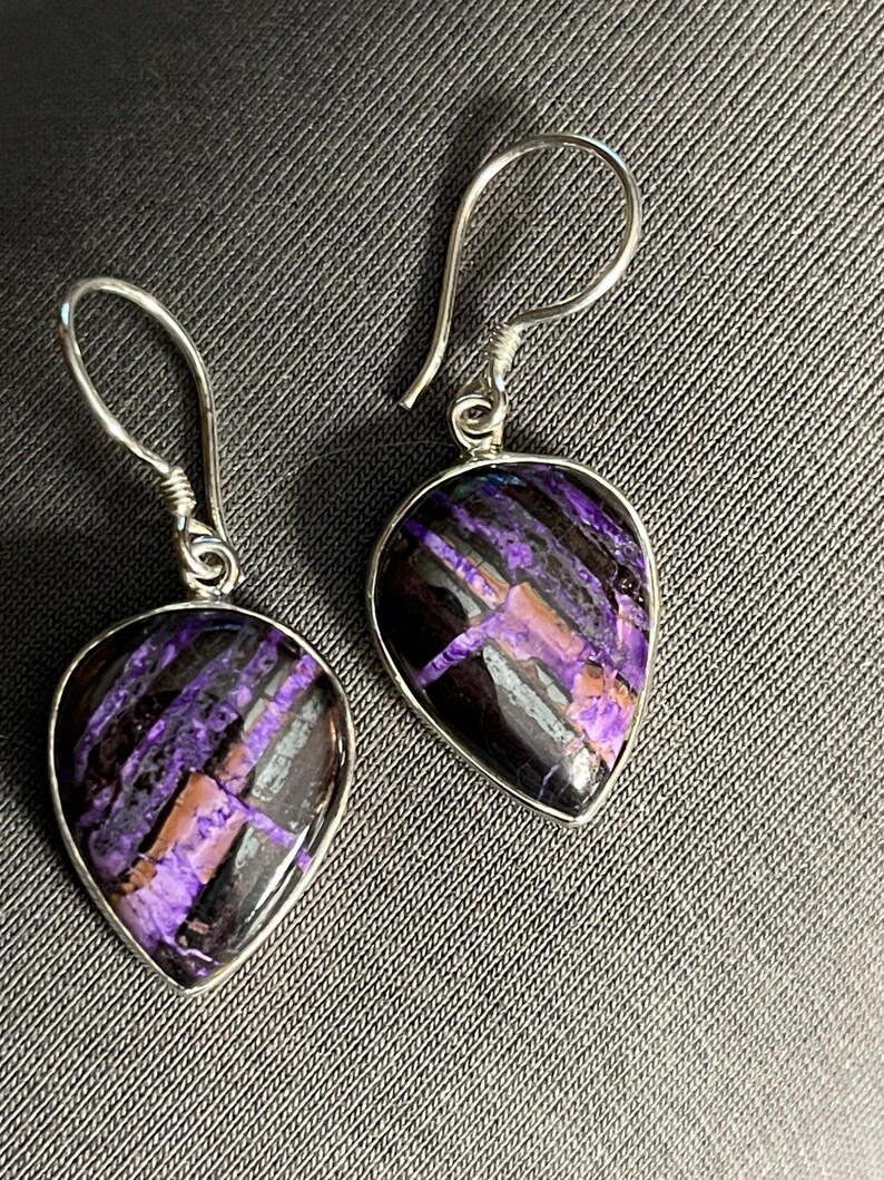 May include: A pair of silver dangle earrings with purple and black teardrop-shaped stones.