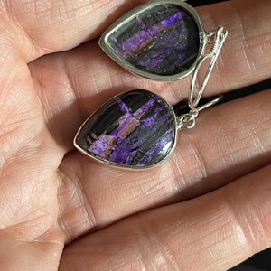 May include: A pair of dangle earrings with teardrop-shaped purple and black stones set in silver.
