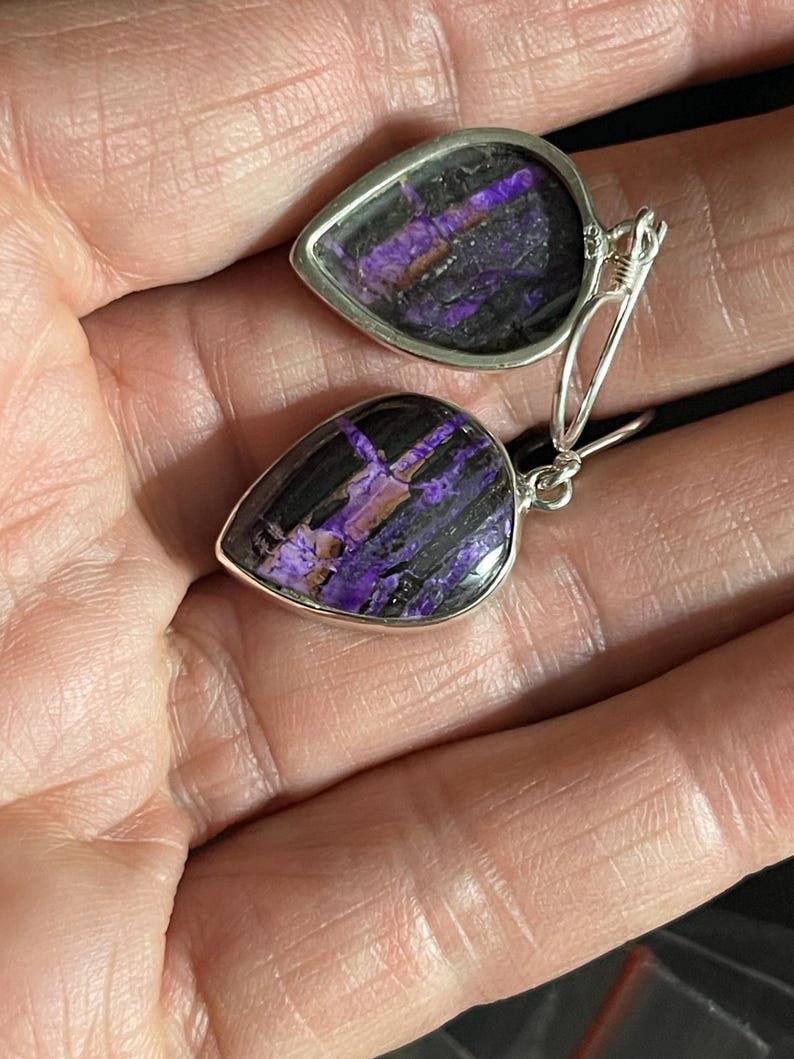 May include: A pair of dangle earrings with teardrop-shaped purple and black stones set in silver.