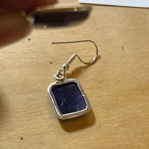 May include: A silver earring with a square-shaped purple stone.