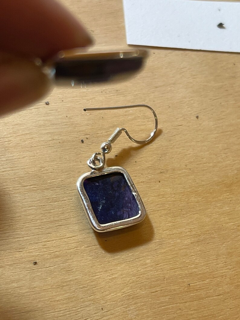 May include: A silver earring with a square-shaped purple stone.