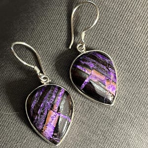May include: A pair of silver dangle earrings with purple and black teardrop-shaped stones.