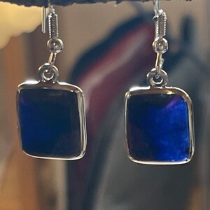 May include: A pair of silver earrings with dark blue square-shaped glass stones.