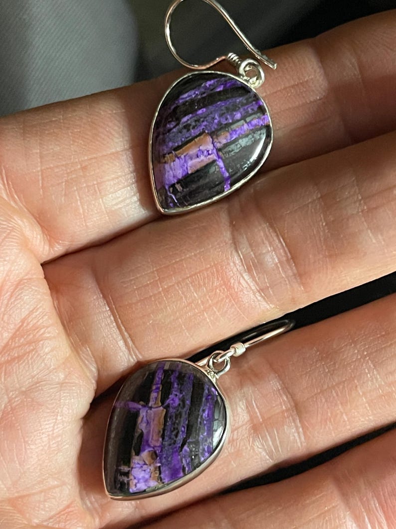May include: A pair of silver dangle earrings with purple and black striped teardrop-shaped stones.
