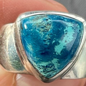 Puede incluir: Un anillo de plata con una piedra preciosa azul triangular. La piedra preciosa tiene un patr&oacute;n moteado de azul claro y oscuro.