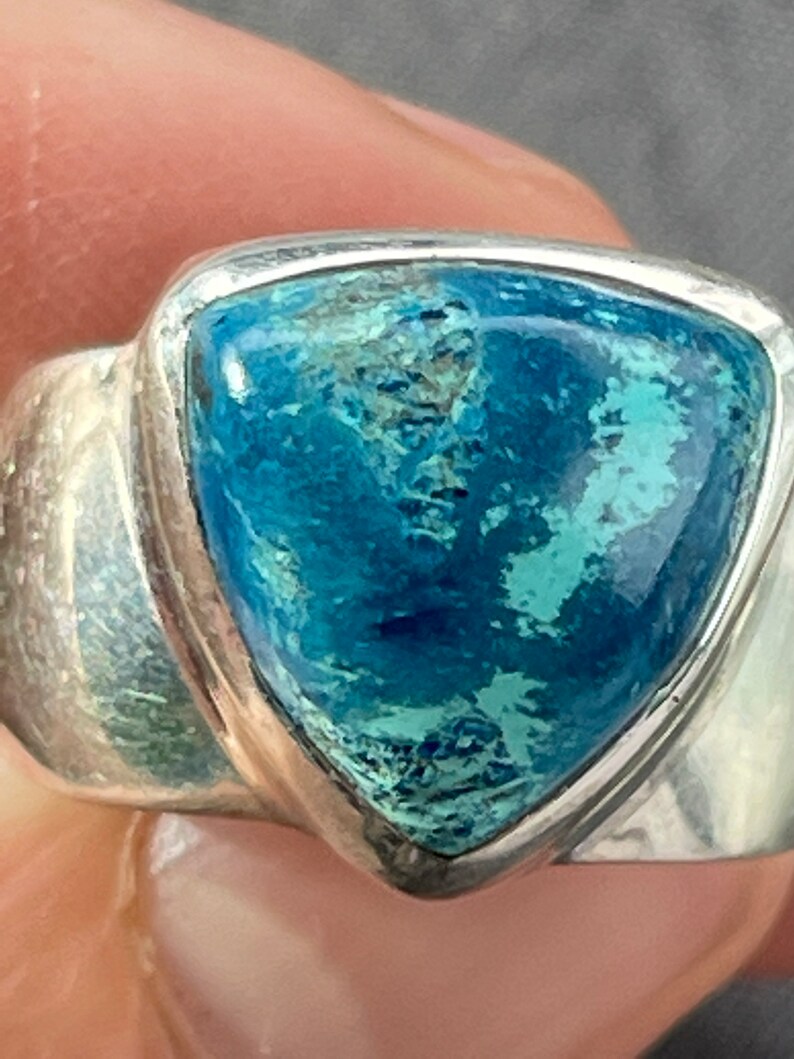 Puede incluir: Un anillo de plata con una piedra preciosa azul triangular. La piedra preciosa tiene un patr&oacute;n moteado de azul claro y oscuro.