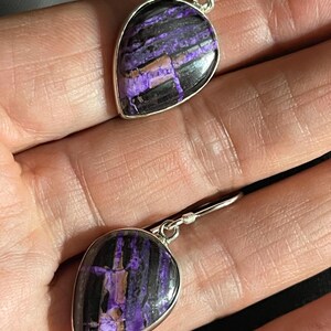 May include: A pair of dangle earrings with a teardrop-shaped purple and black stone set in silver.