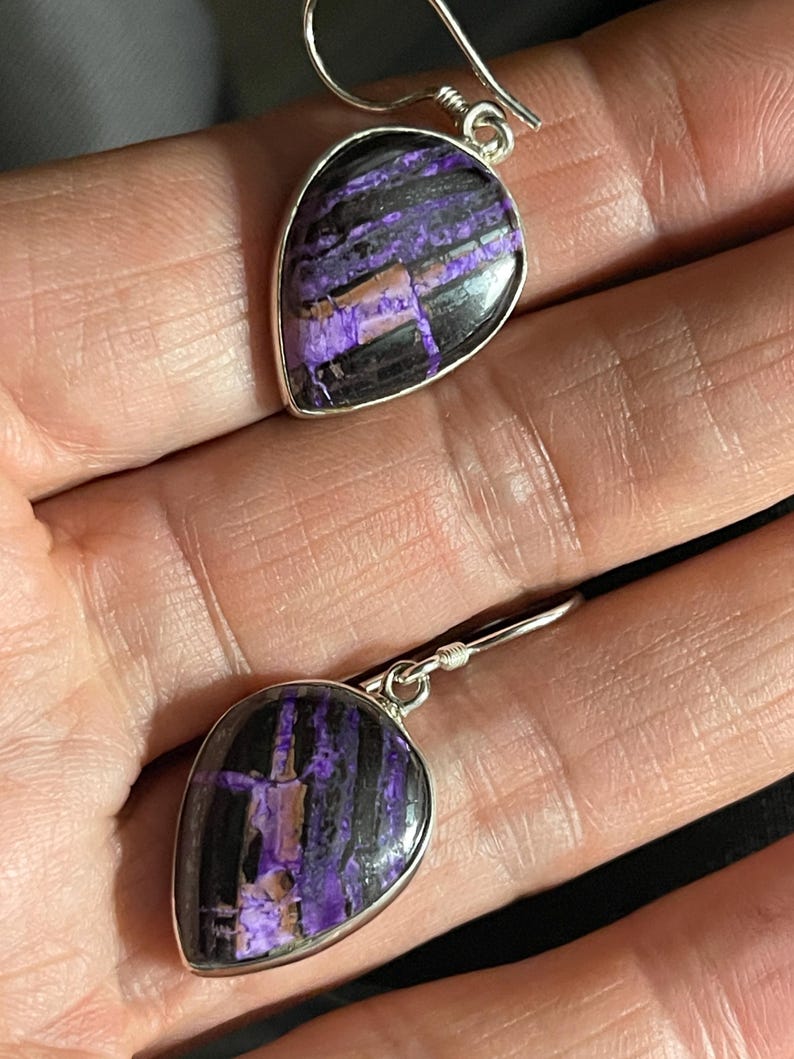 May include: A pair of dangle earrings with a teardrop-shaped purple and black stone set in silver.