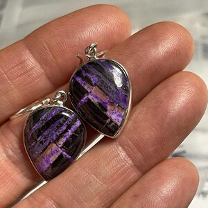 May include: A pair of silver earrings with purple and black striped gemstone drops.