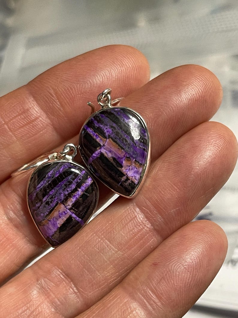 May include: A pair of silver earrings with purple and black striped gemstone drops.