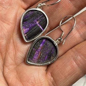 May include: A pair of silver dangle earrings with purple and black stone teardrop shaped pendants.