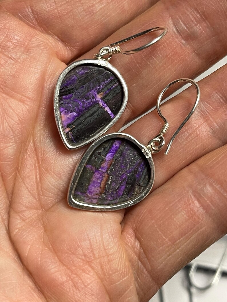 May include: A pair of silver dangle earrings with purple and black stone teardrop shaped pendants.