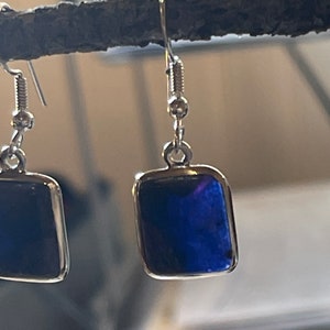 May include: A pair of silver earrings with a square blue stone. The earrings have a simple design and are perfect for everyday wear.