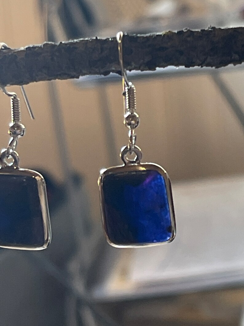 May include: A pair of silver earrings with a square blue stone. The earrings have a simple design and are perfect for everyday wear.