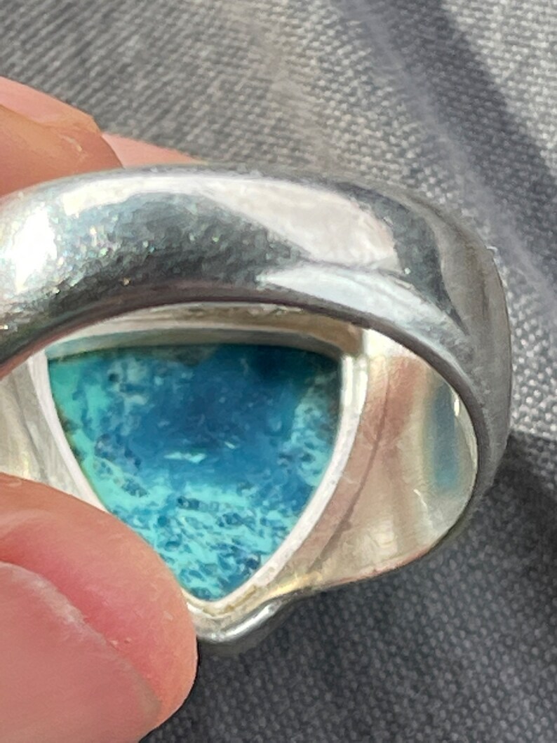 Puede incluir: Un anillo de plata con una piedra preciosa azul y verde engastada en forma triangular.
