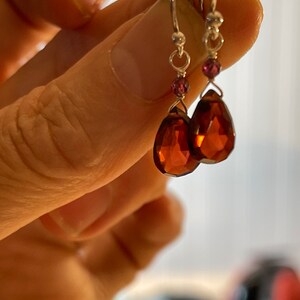 May include: A pair of silver dangle earrings with teardrop-shaped brown gemstones and small pink accent beads.
