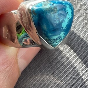Puede incluir: Un anillo de plata con una piedra preciosa azul triangular. La piedra preciosa tiene un patr&oacute;n moteado y est&aacute; engastada en una banda de plata.