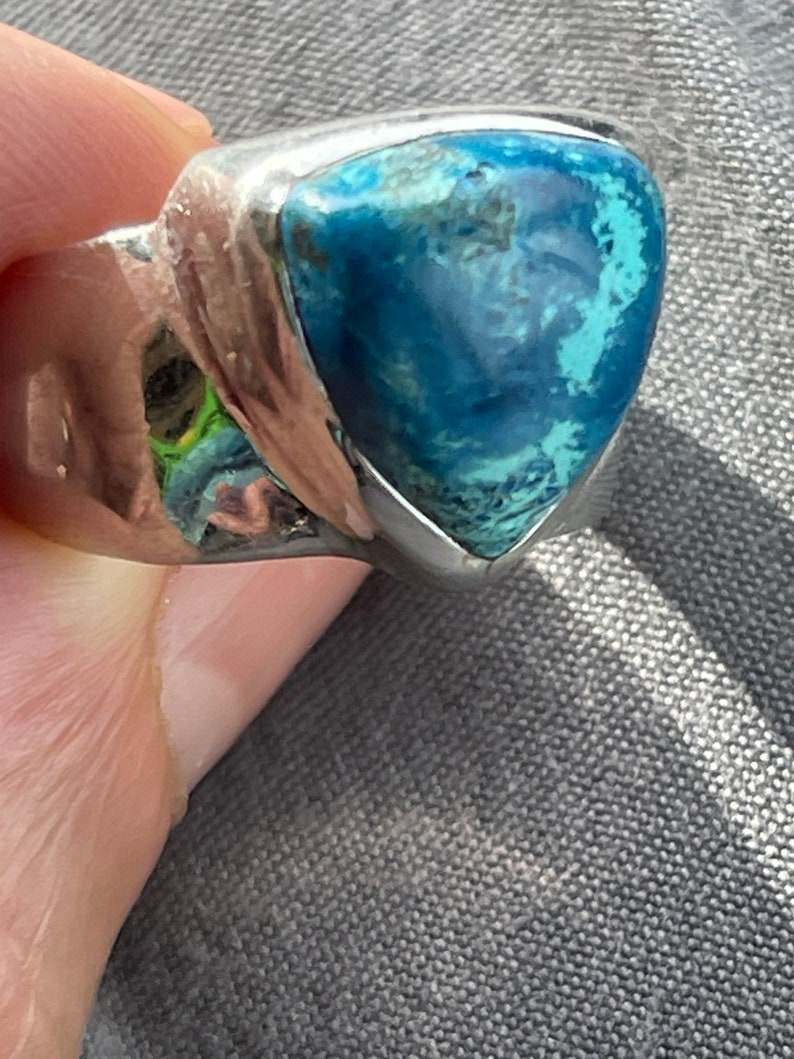 Puede incluir: Un anillo de plata con una piedra preciosa azul triangular. La piedra preciosa tiene un patr&oacute;n moteado y est&aacute; engastada en una banda de plata.