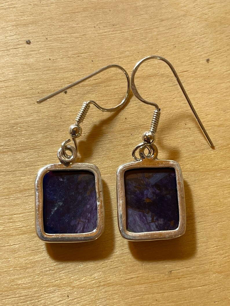 May include: A pair of silver earrings with square-shaped purple and silver stones.