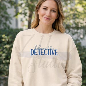 Peut inclure: Sweat-shirt crème avec l'inscription bleue "life on the DETECTIVE Studio". Ce vêtement à manches longues et col rond présente un motif centré sur le devant.