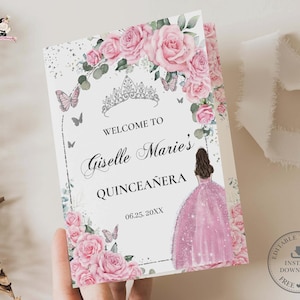 Peut inclure: Une carte d'invitation pliée avec un motif floral. La carte présente des roses roses, des papillons et un diadème. Le texte indique "Welcome to Giselle Marie's Quinceañera" avec une date. Un dessin d'une fille en robe rose est également inclus.