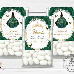 Puede incluir: Tres recipientes de plástico transparente llenos de mentas blancas. Cada recipiente tiene una etiqueta con un diseño floral verde y dorado, una ilustración de vestido de quinceañera y el texto "Adriana's Quinceañera". El recipiente central dice "Gracias".