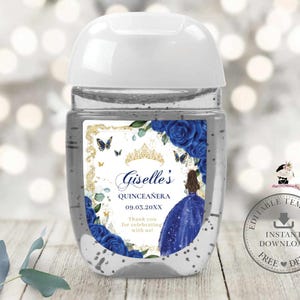 May include: A clear hand sanitizer bottle with a white cap. The label features a gold frame with blue roses, butterflies, and a tiara. The text reads "Giselle's Quinceañera 09.03.20XX" and "Thank you for celebrating with us!"