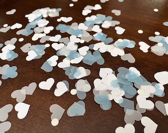 May include: A scattering of blue and white heart-shaped confetti on a brown wooden surface.