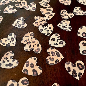 May include: A scattering of brown and tan leopard print heart-shaped confetti on a dark brown surface.