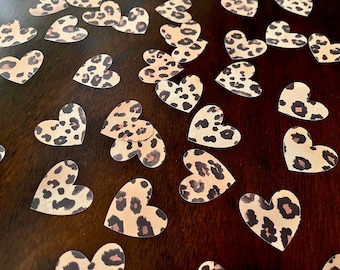 May include: A scattering of brown and tan leopard print heart-shaped confetti on a dark brown surface.