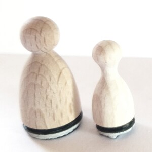 May include: Two wooden stamps shaped like people, one larger than the other. Both stamps have a black and white base.