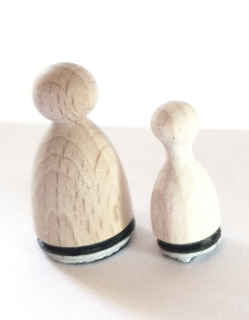 May include: Two wooden stamps shaped like people, one larger than the other. Both stamps have a black and white base.
