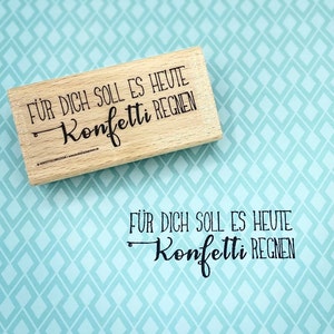 May include: A wooden stamp with the text "Für dich soll es heute Konfetti regnen" in black lettering. The stamp is on a light blue background with a diamond pattern.