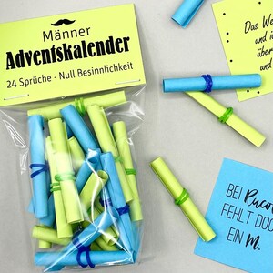 Puede incluir: Una bolsa transparente llena de rollos de papel azul y verde, asegurados con bandas elásticas. La bolsa está etiquetada como "Männer Adventskalender" con texto debajo. Hay rollos y notas adhesivas adicionales dispersos.
