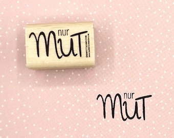Può includere: Un timbro di legno con il testo "nur Mut" in lettere nere. Il timbro è su uno sfondo rosa con pois bianchi.