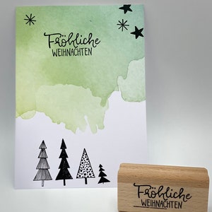 Peut inclure: Un tampon en caoutchouc en bois avec le texte "Fr&ouml;hliche Weihnachten" en lettres noires. Le tampon est sur une surface blanche.