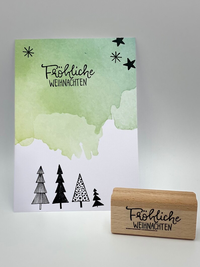 Peut inclure: Un tampon en caoutchouc en bois avec le texte "Fr&ouml;hliche Weihnachten" en lettres noires. Le tampon est sur une surface blanche.