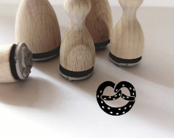 May include: Four wooden stamps with black ink pads, one of which has been used to create a black and white image of a pretzel on a white surface.