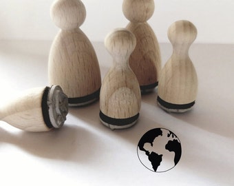 May include: Five wooden stamps with black ink pads, shaped like people, with a black and white globe stamp imprint on a white surface.