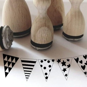 May include: Five wooden stamps with black ink pads, each featuring a different black and white geometric pattern: triangles, stripes, polka dots, stars, and hearts. The stamps are arranged in a row on a white surface.